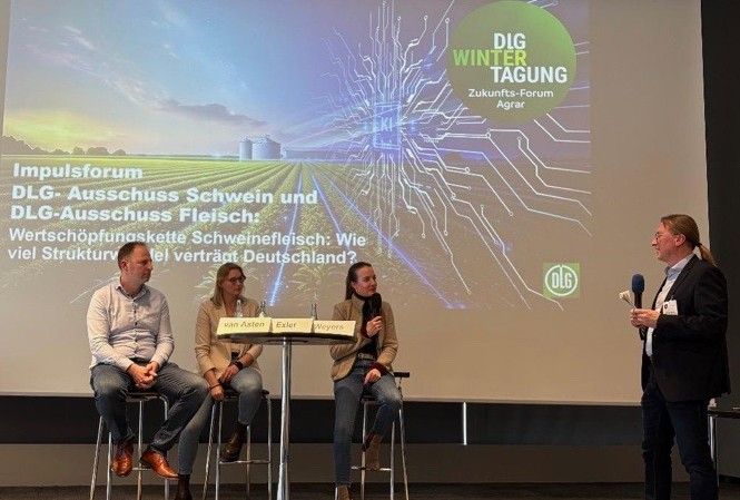 Vier Personen sitzen auf einem Podium der DLG-Wintertagung Landwirtschaft. Ein Moderator mit Mikrofon spricht zu den drei Podiumsteilnehmern, während hinter ihnen ein großer Bildschirm die Veranstaltungshinweise und den "Automatisch gespeicherten Entwurf" anzeigt.